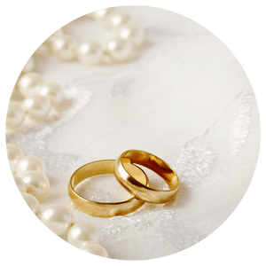 wedding rings on embroidered white background surrounded by pearls