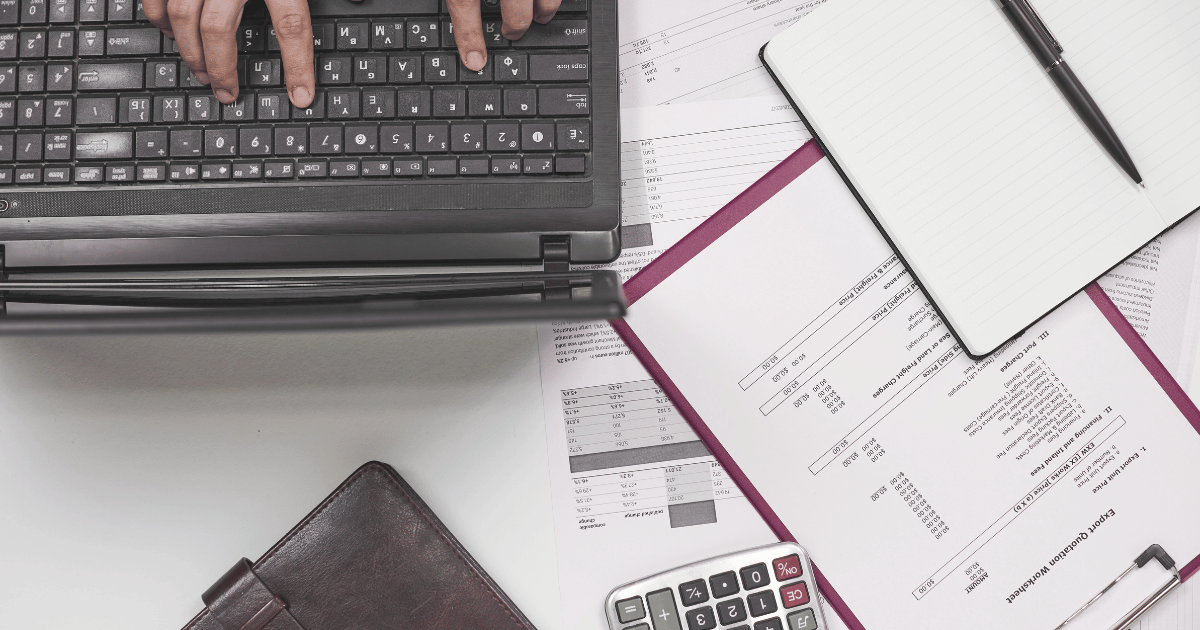 flatlay image of a laptop and assorted import papers and calculator